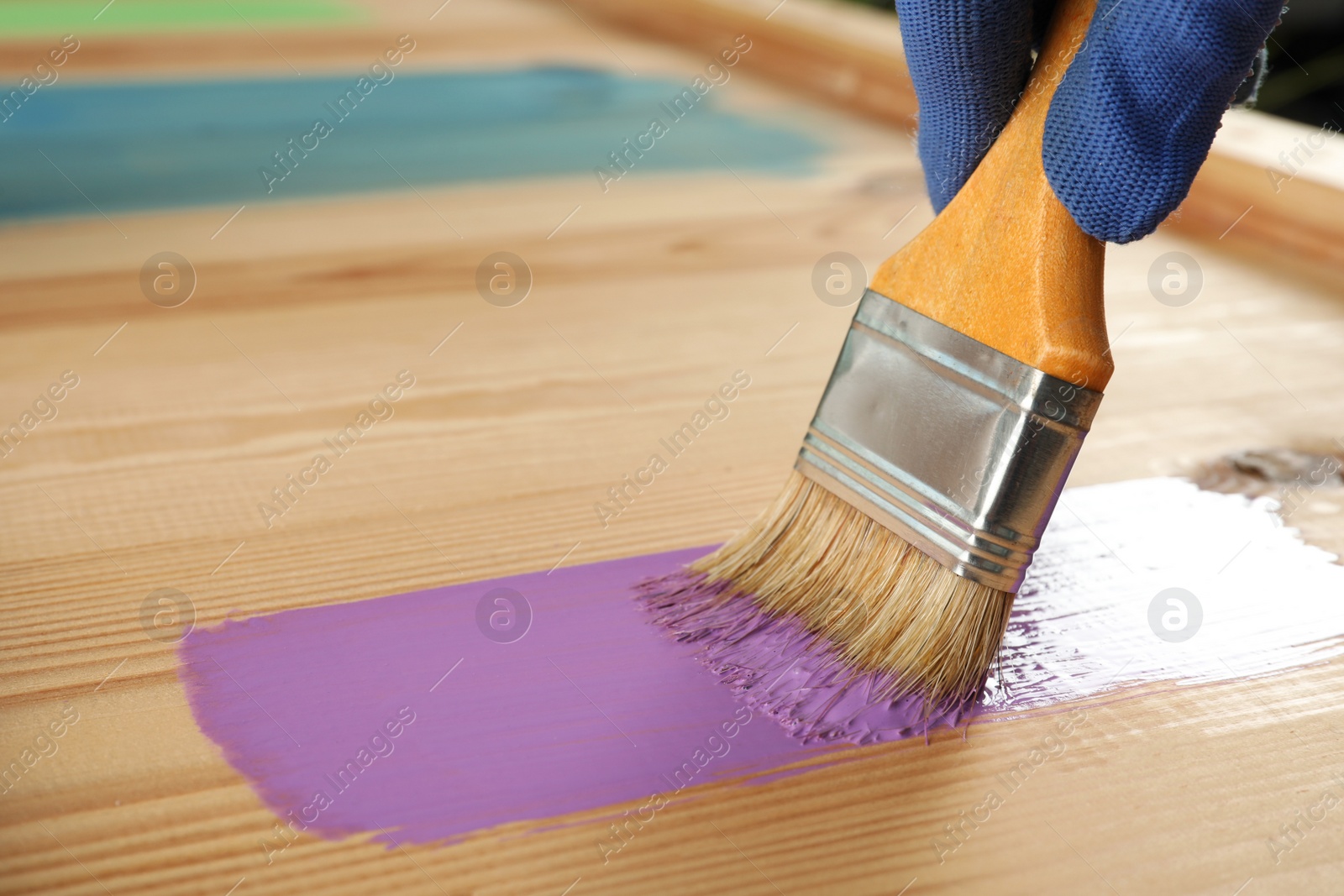 Photo of Worker applying violet paint onto wooden surface, closeup. Space for text