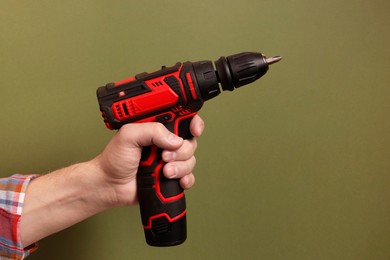 Handyman holding electric screwdriver on olive background, closeup