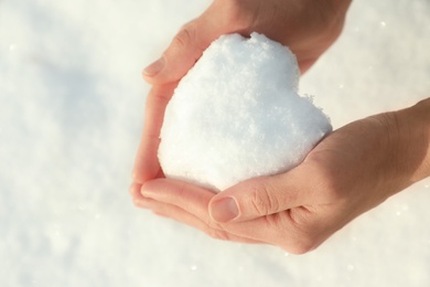 Photo of Woman holding heart made of snow outdoors, closeup. Space for text