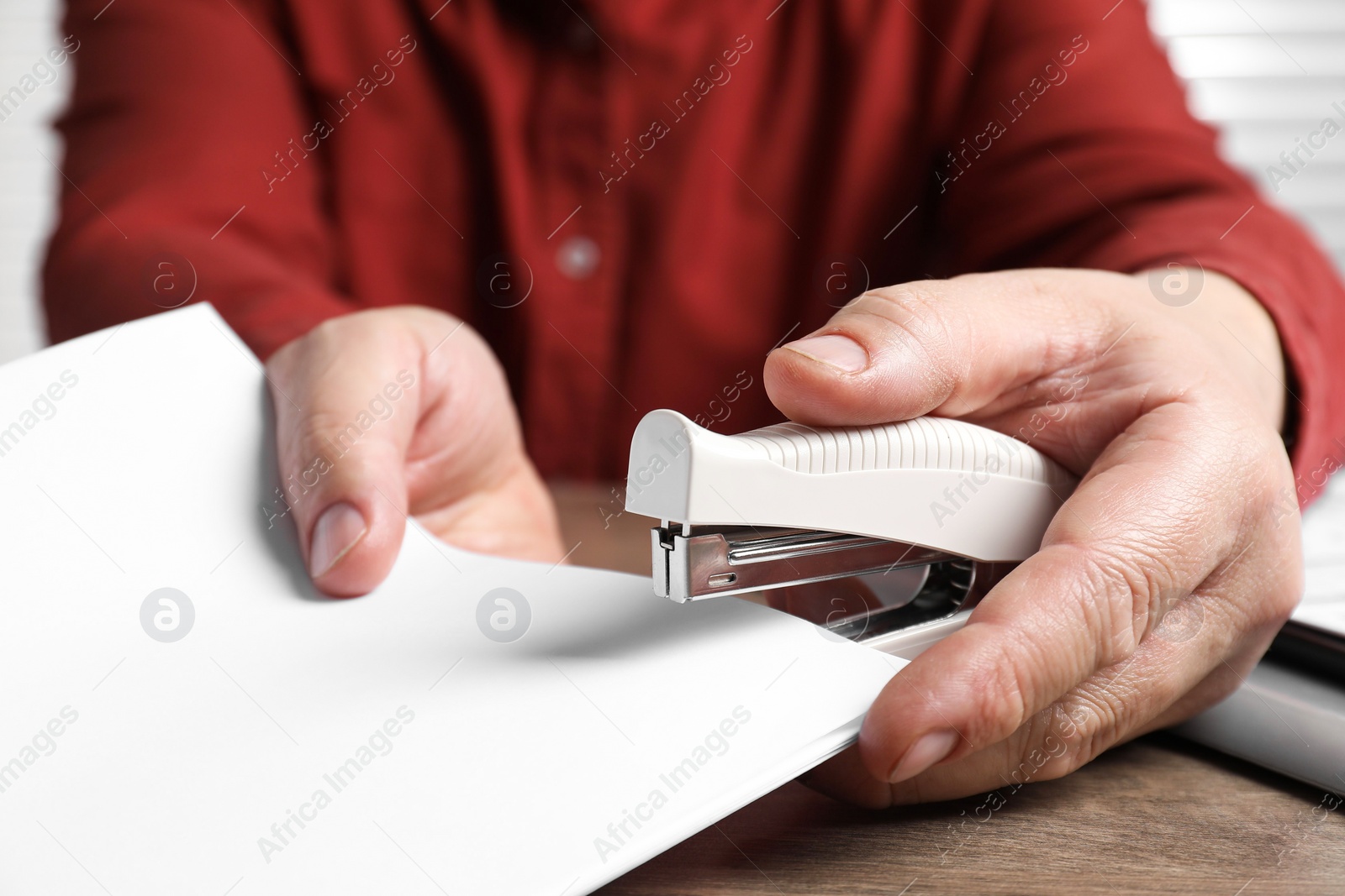 Photo of Man stapling papers at wooden table, closeup