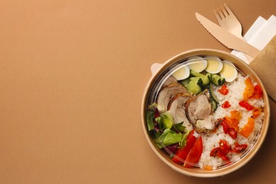 Photo of Tasty food in container with wooden fork and knife on beige background, flat lay. Space for text