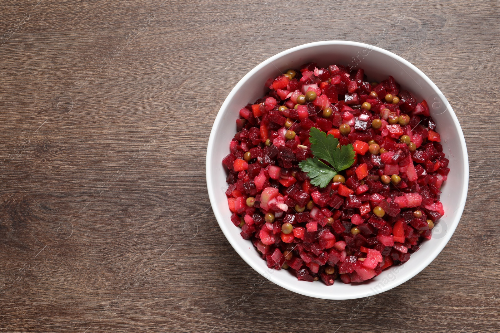 Photo of Bowl of delicious fresh vinaigrette salad on wooden table, top view. Space for text