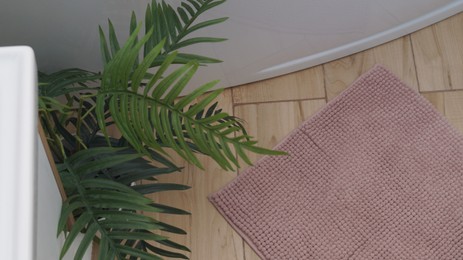 Photo of Soft bath mat near houseplant and tub on wooden floor in bathroom, above view