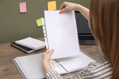 Photo of Woman putting paper sheet into punched pocket at wooden table, closeup