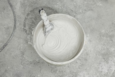 Photo of Bucket with plaster and putty knife on concrete floor, top view