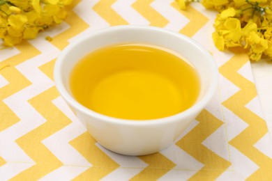 Rapeseed oil in bowl and beautiful yellow flowers on table, closeup