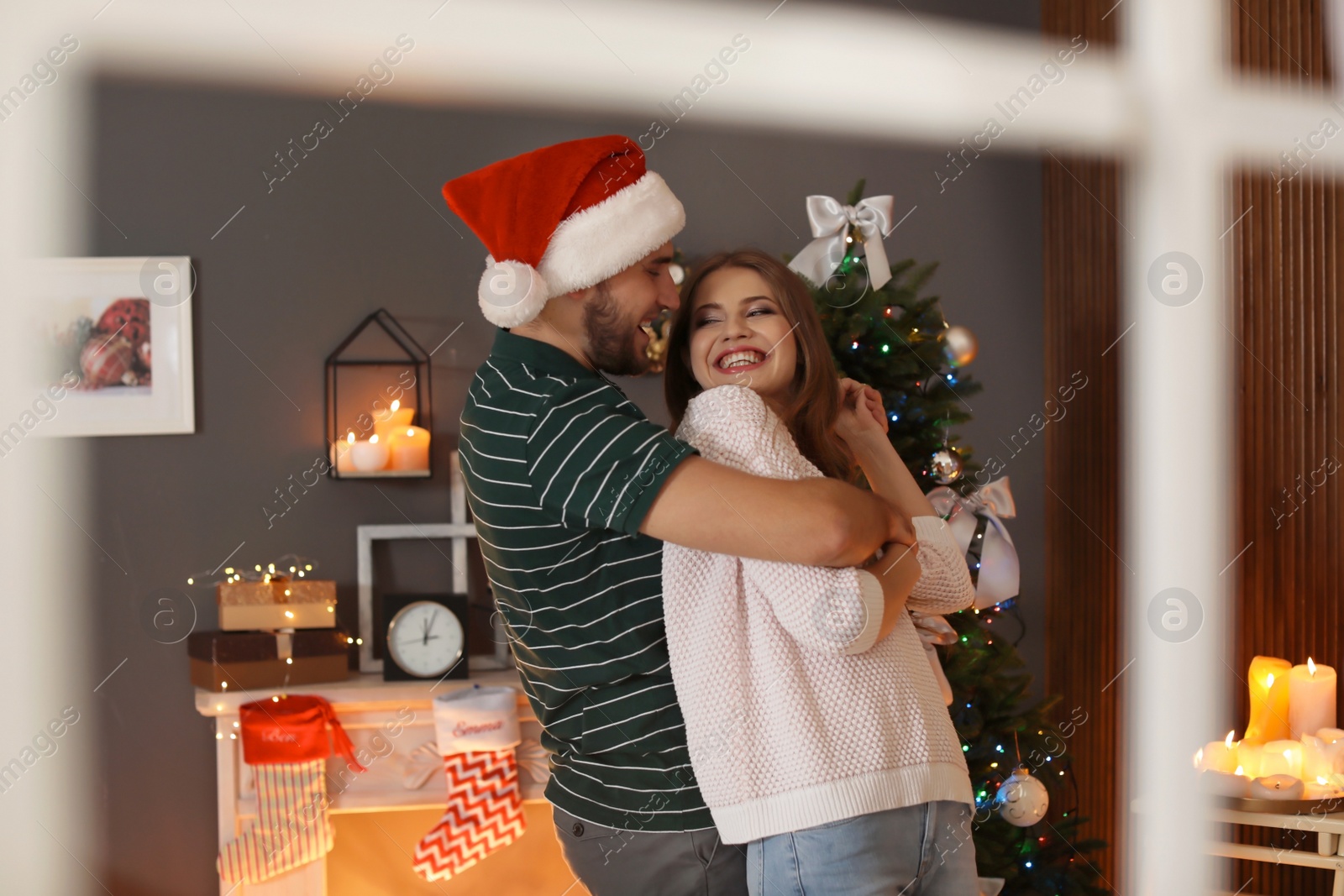 Photo of Happy young couple celebrating Christmas at home, view from outside