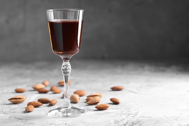 Photo of Liqueur glass with tasty amaretto and almonds on light grey table, closeup. Space for text
