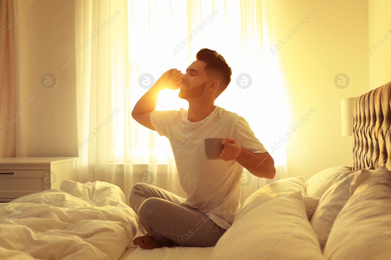 Photo of Young man with cup of coffee on bed at home. Lazy morning