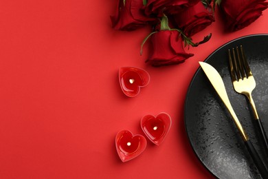 Photo of Place setting with heart shaped candles and bouquet of roses for romantic dinner on red table, flat lay. Space for text