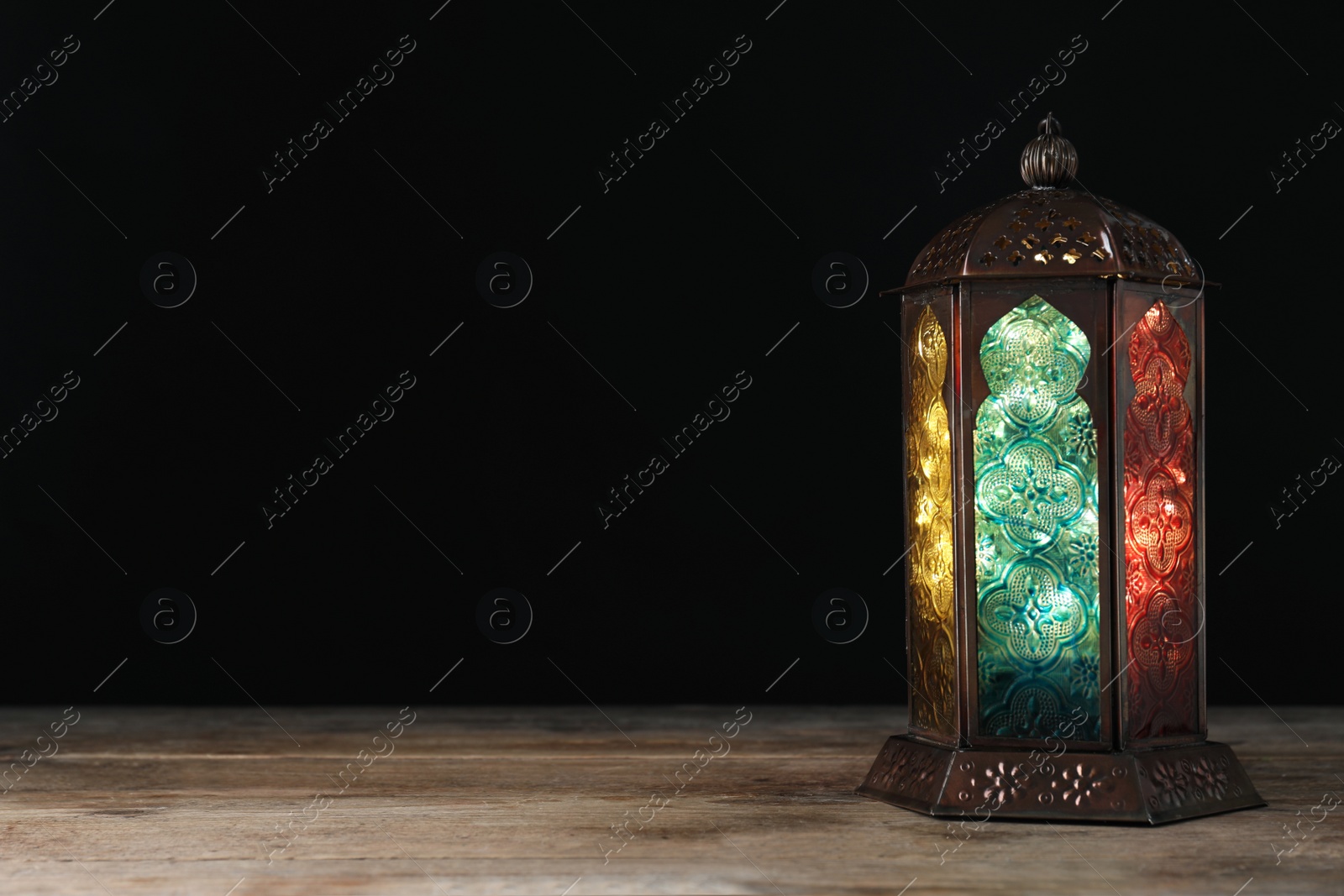 Photo of Decorative Arabic lantern on wooden table against black background, space for text