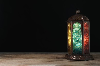Photo of Decorative Arabic lantern on wooden table against black background, space for text