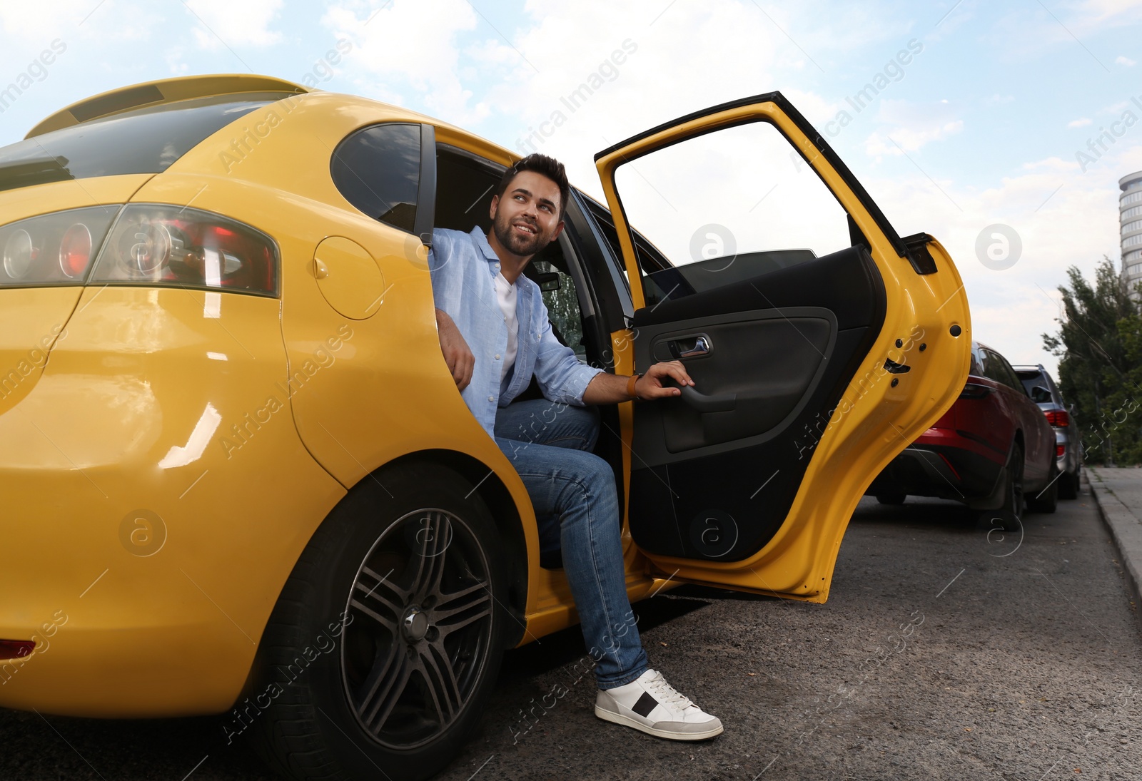 Photo of Handsome young man getting out of taxi on city street