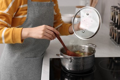 Woman cooking soup on cooktop in kitchen, closeup