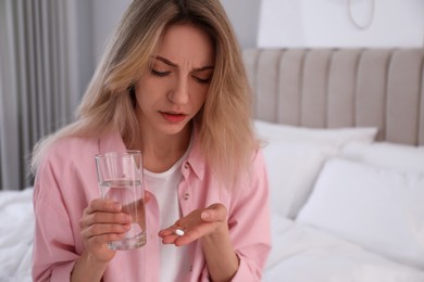 Photo of Upset young woman with abortion pill and glass of water at home