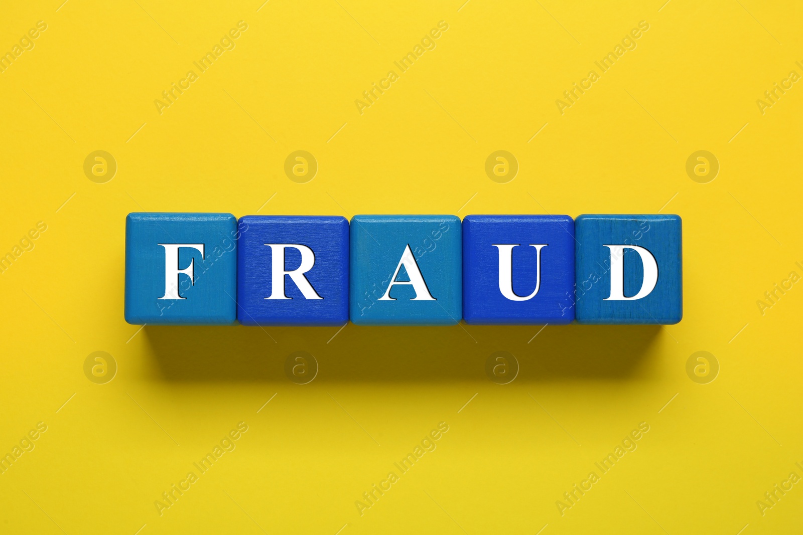 Photo of Word Fraud of wooden cubes with letters on yellow background, flat lay