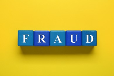 Photo of Word Fraud of wooden cubes with letters on yellow background, flat lay
