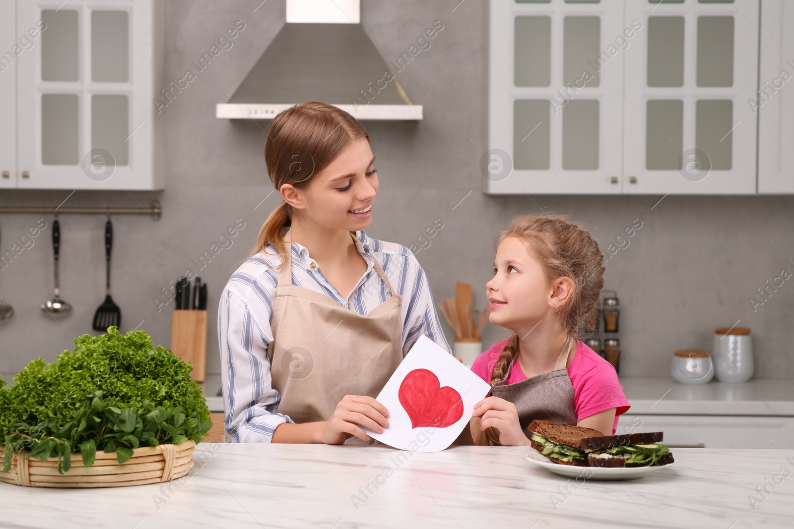 Photo of Little daughter congratulating mom with greeting card in kitchen. Happy Mother's Day