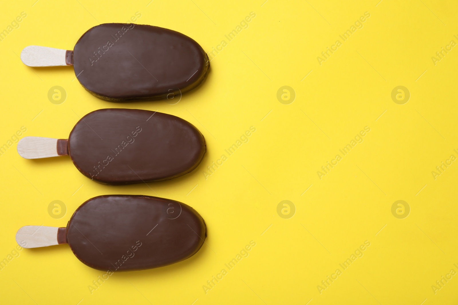 Photo of Glazed ice cream bars on yellow background, flat lay. Space for text