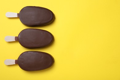 Glazed ice cream bars on yellow background, flat lay. Space for text