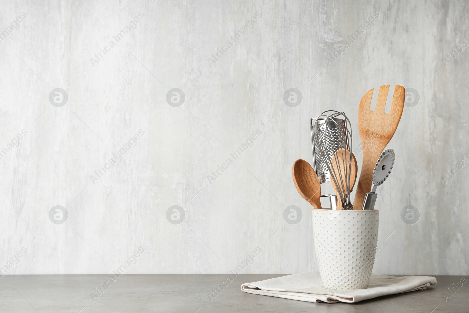 Photo of Holder with kitchen utensils on grey table against light background. Space for text