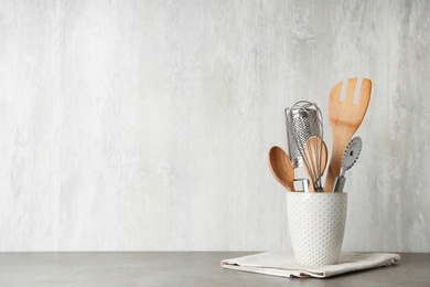 Photo of Holder with kitchen utensils on grey table against light background. Space for text