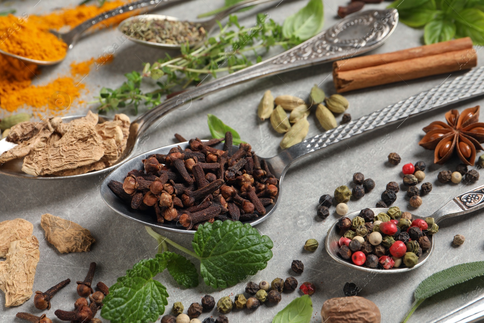 Photo of Different herbs and spices with spoons on grey table, closeup