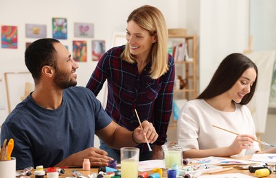 Artist teaching her students to paint at table in studio. Creative hobby