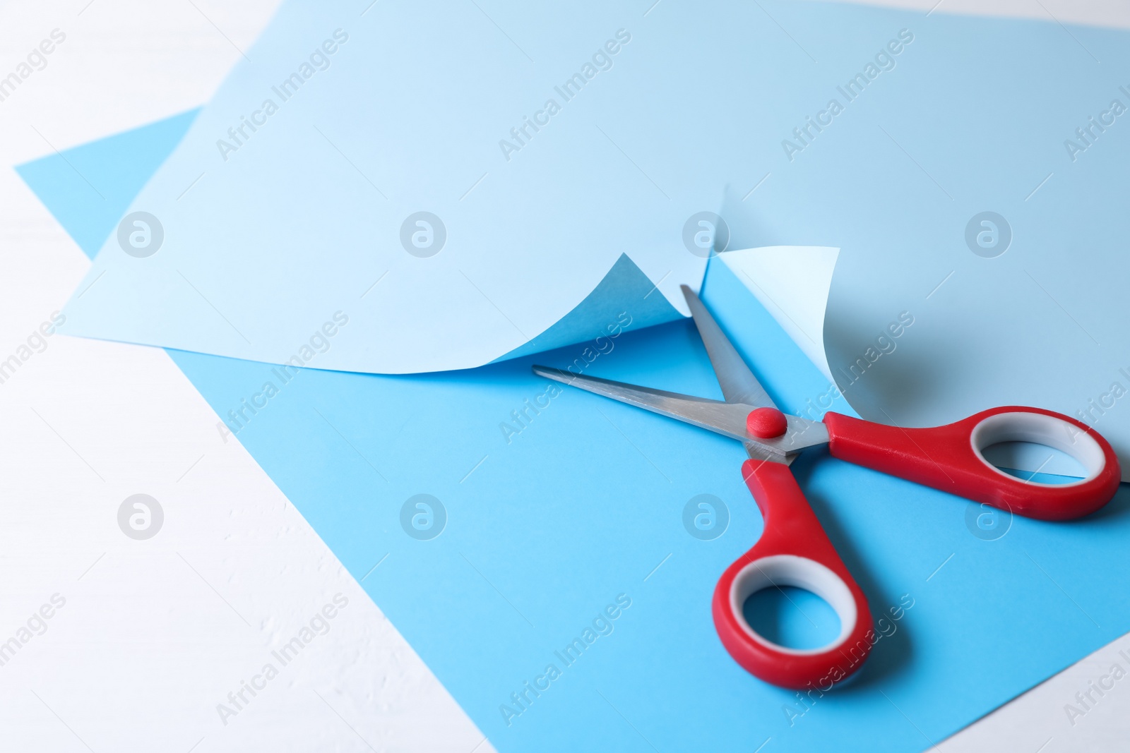 Photo of Red scissors and light blue paper on white background