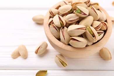 Photo of Tasty pistachios in bowl on white wooden table, closeup. Space for text