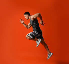 Athletic young man running on red background, side view