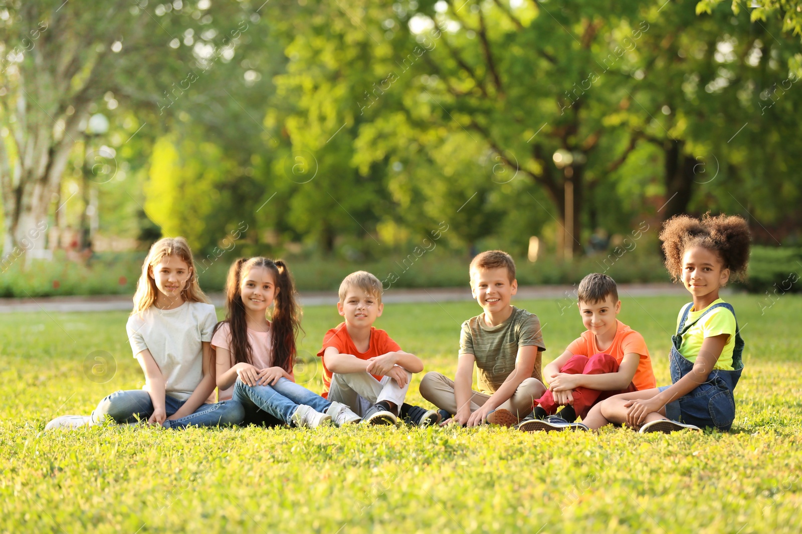 Photo of Cute little children sitting on grass outdoors on sunny day