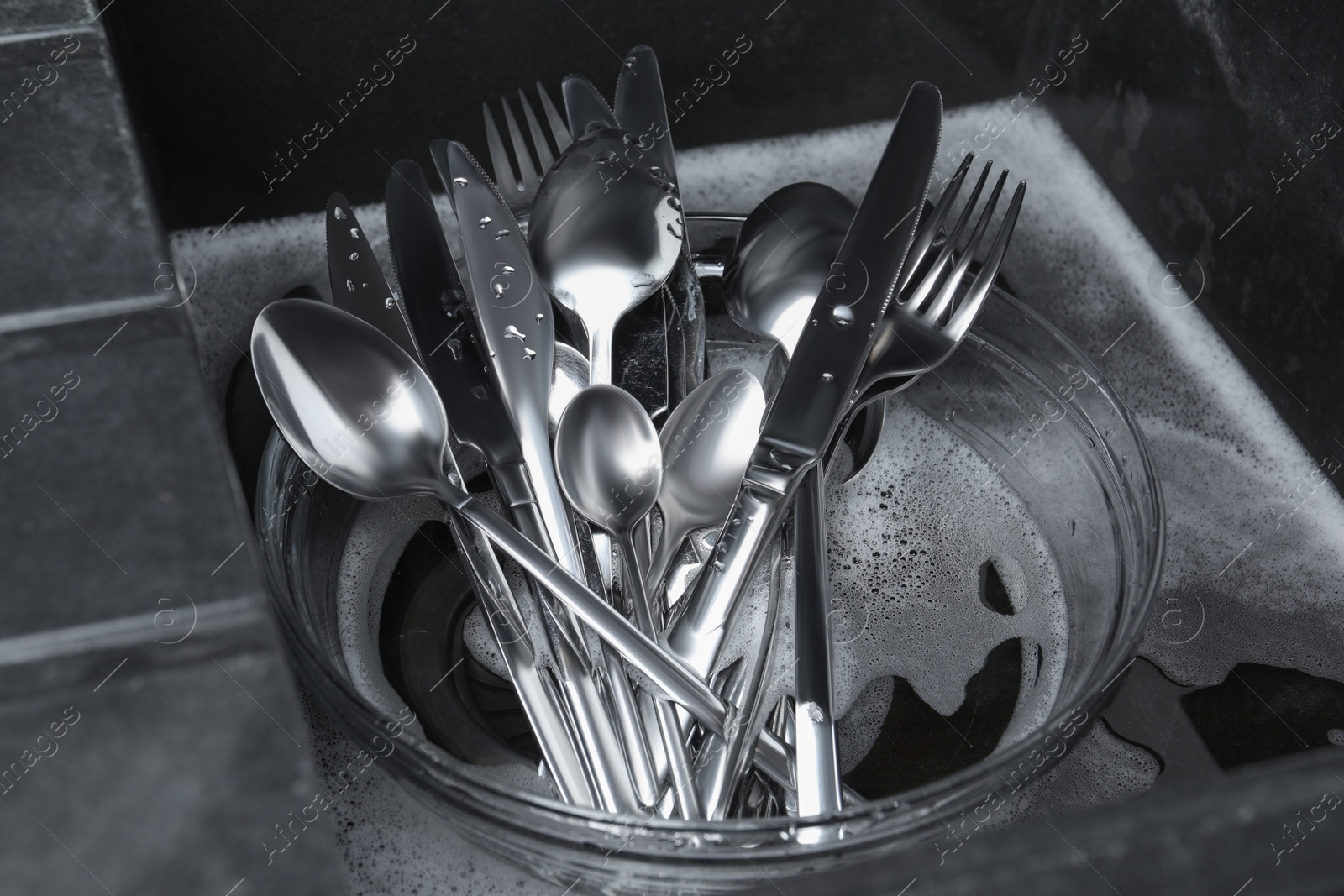 Photo of Washing silver spoons, forks and knives in kitchen sink with foam, above view