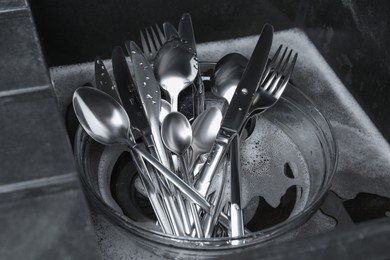 Washing silver spoons, forks and knives in kitchen sink with foam, above view