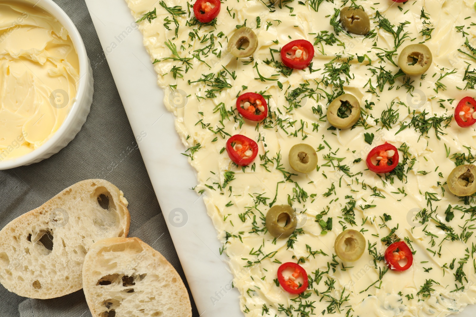 Photo of Fresh butter board with cut olives, pepper and bread on grey tablecloth, flat lay