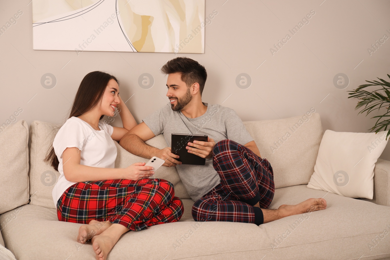 Photo of Happy couple in pajamas with gadgets on sofa at home