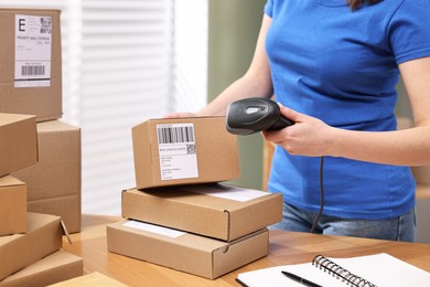 Photo of Parcel packing. Post office worker with scanner reading barcode indoors, closeup