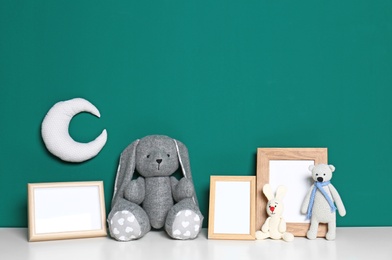 Photo of Soft toys and photo frames on table against green background, space for text. Child room interior