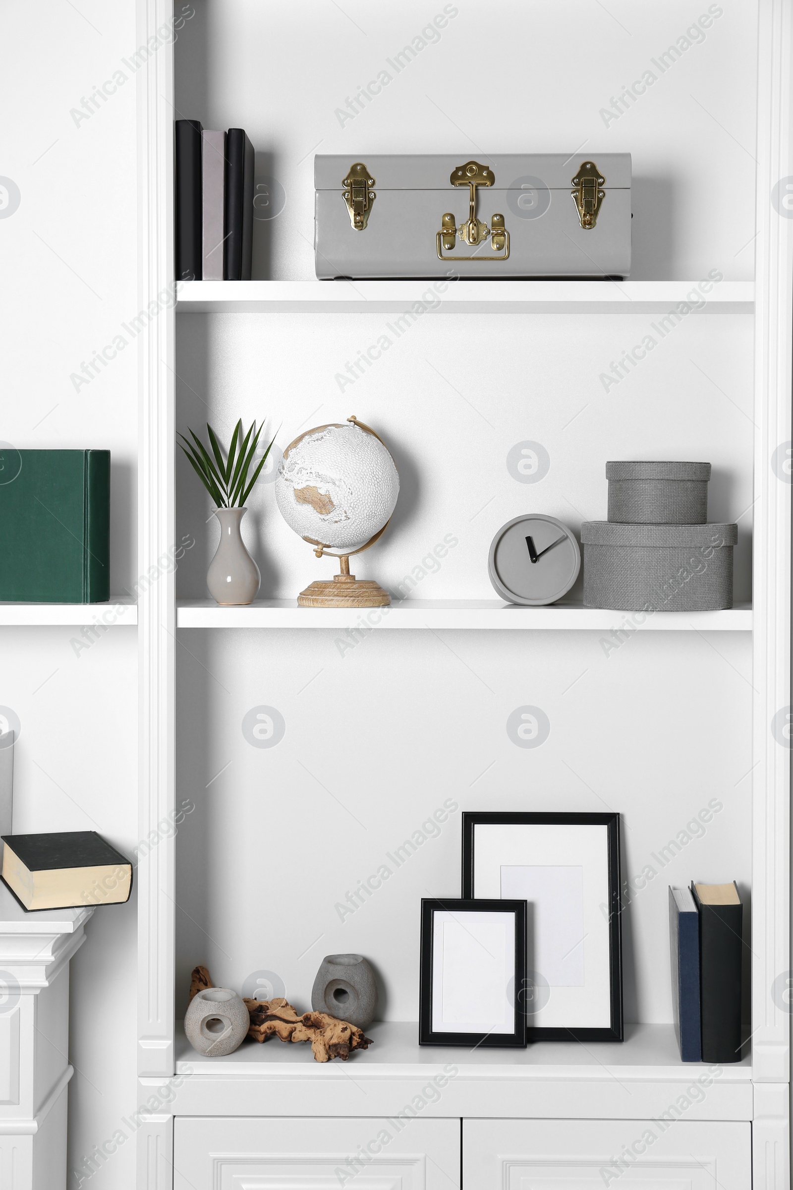 Photo of White shelves with books, clock and different decor indoors. Interior design