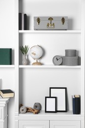 White shelves with books, clock and different decor indoors. Interior design