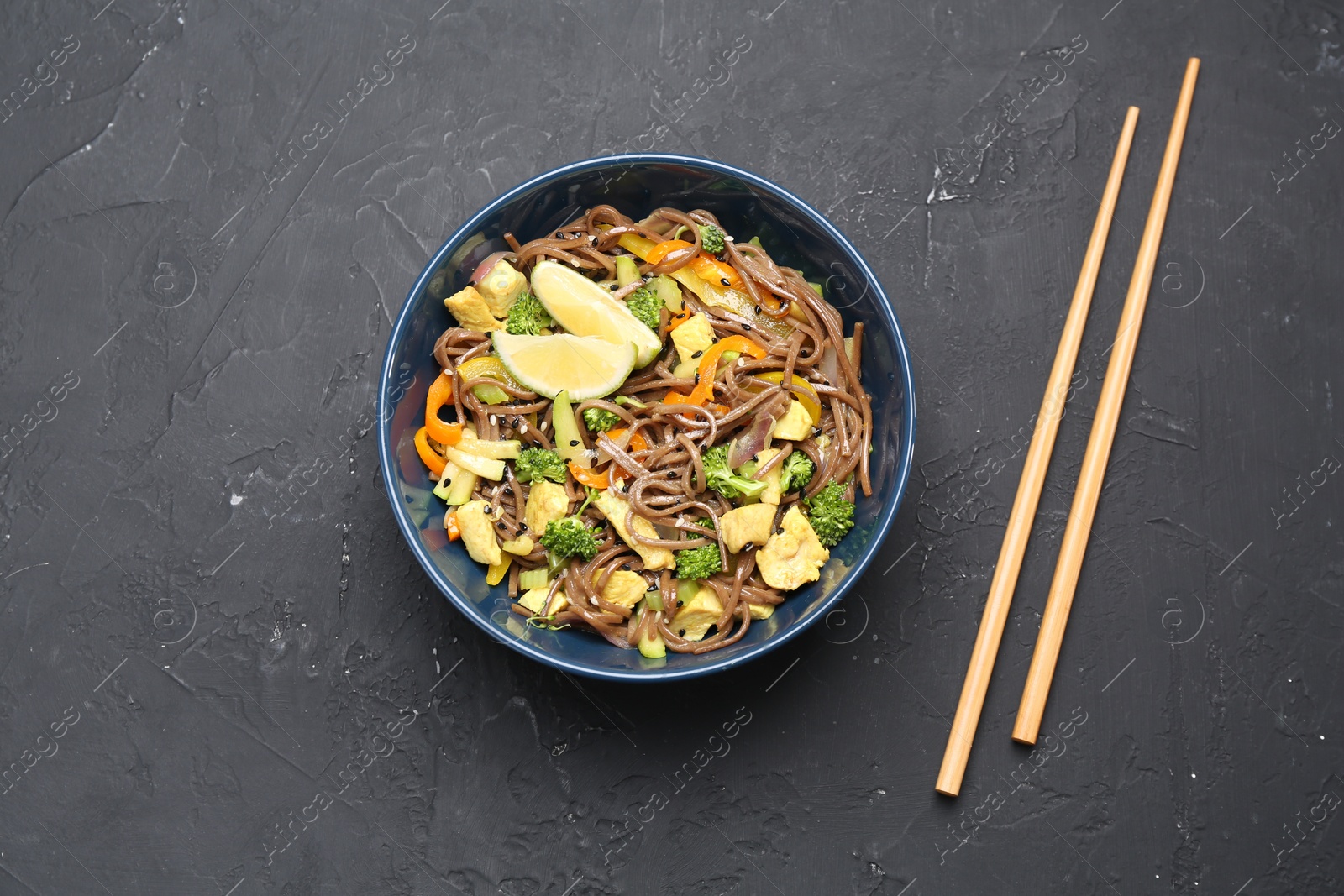 Photo of Stir-fry. Delicious cooked noodles with chicken and vegetables in bowl served on gray textured table, flat lay