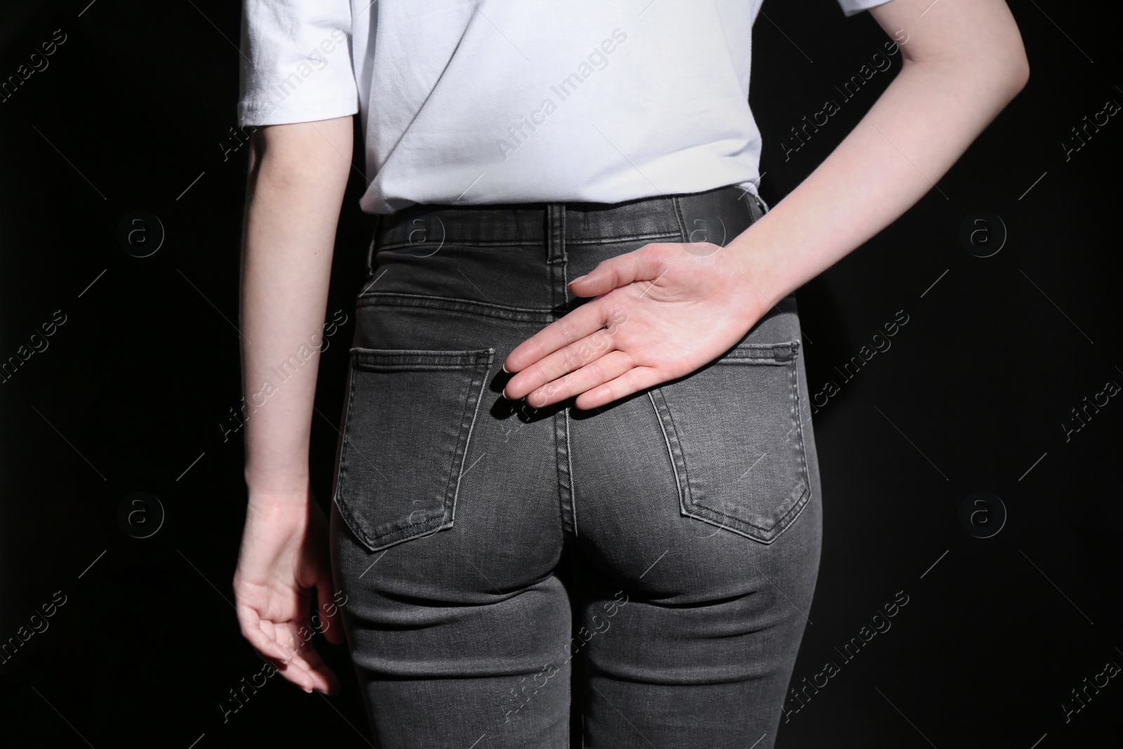 Photo of Woman showing open palm behind her back on black background, back view