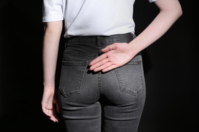 Woman showing open palm behind her back on black background, back view