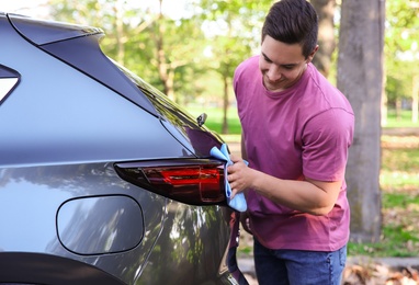 Photo of Young man washing car rear light with rag outdoors