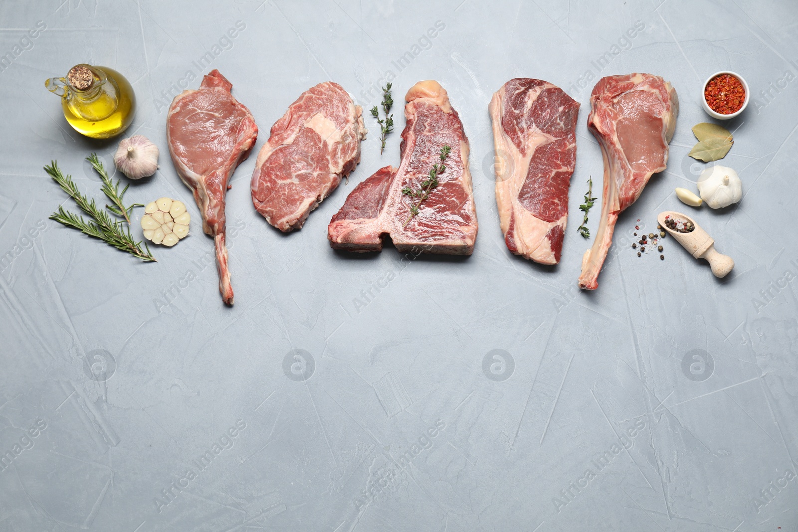 Photo of Fresh raw beef cuts, spices and oil on light grey textured table, flat lay. Space for text