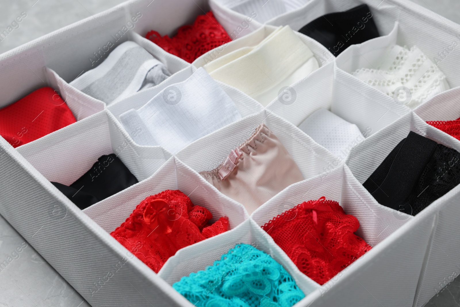 Photo of Organizer with folded women's underwear on light grey table, closeup