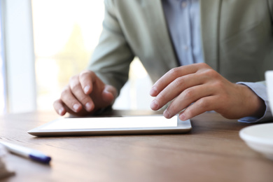 Photo of Businessman working with modern tablet at wooden table in office, closeup