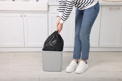 Photo of Woman taking garbage bag out of trash bin in kitchen, closeup