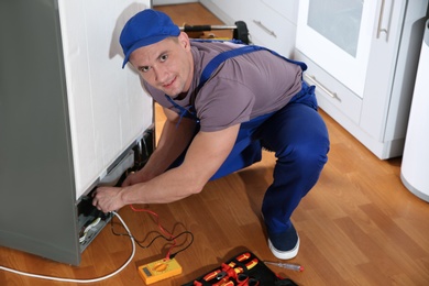 Male technician in uniform repairing refrigerator indoors