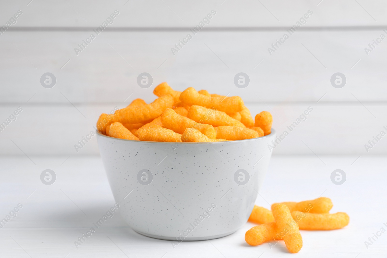 Photo of Bowl with crunchy cheesy corn snack on white table, closeup